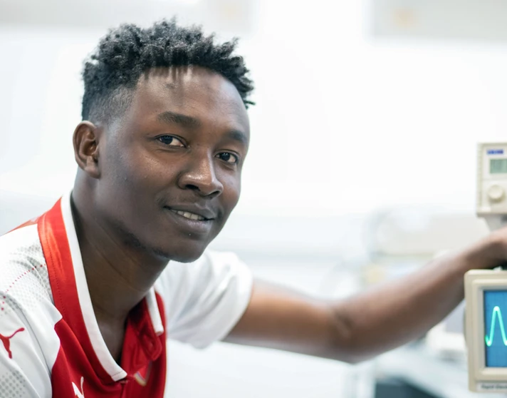 Close-up of a student in a red football jersey adjusting an oscilloscope, displaying a waveform on the screen. Close-up of a student in a red football jersey adjusting an oscilloscope, displaying a waveform on the screen.
